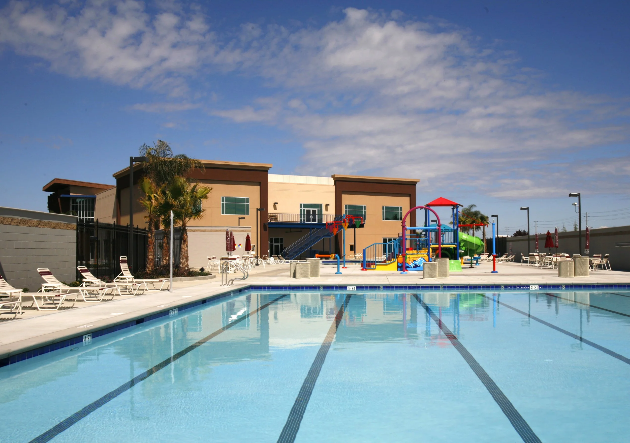 The outdoor aquatic center, a marked lap pool with loungers along the far side and the play structure beyond.