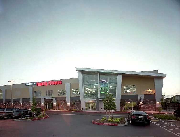 At dusk from across the parking lot, a low wide block with a pale swept roof edge and light behind the glazing.
