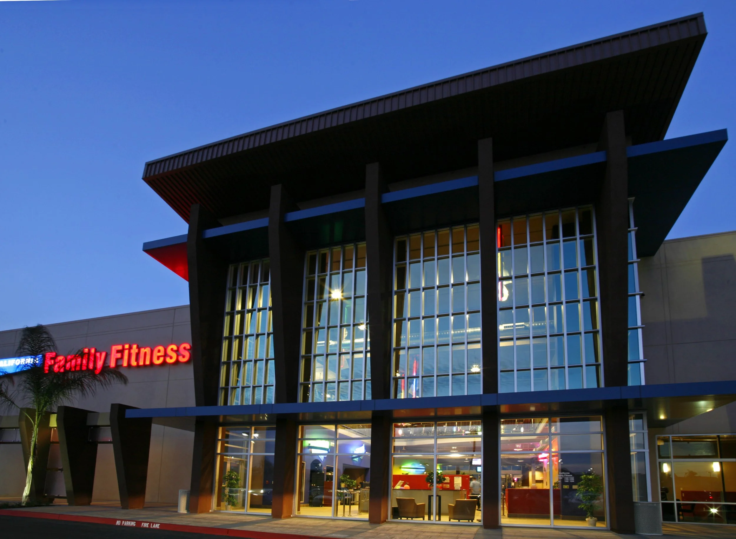 The club at dusk, its glazed entry tower lit warm between deep timber piers under a flat oversailing roof.
