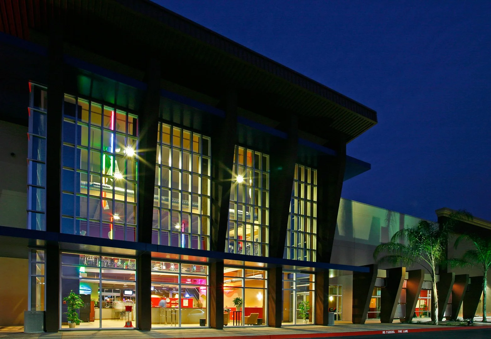 The same tower close in, its glazing a lit grid of colour behind dark timber mullions.