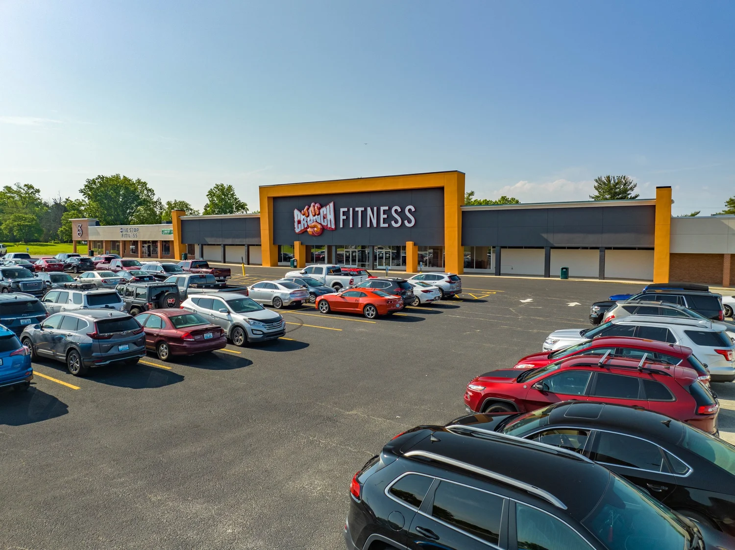 A storefront framed in orange with the Crunch Fitness sign above the doors, the parking lot full of cars.