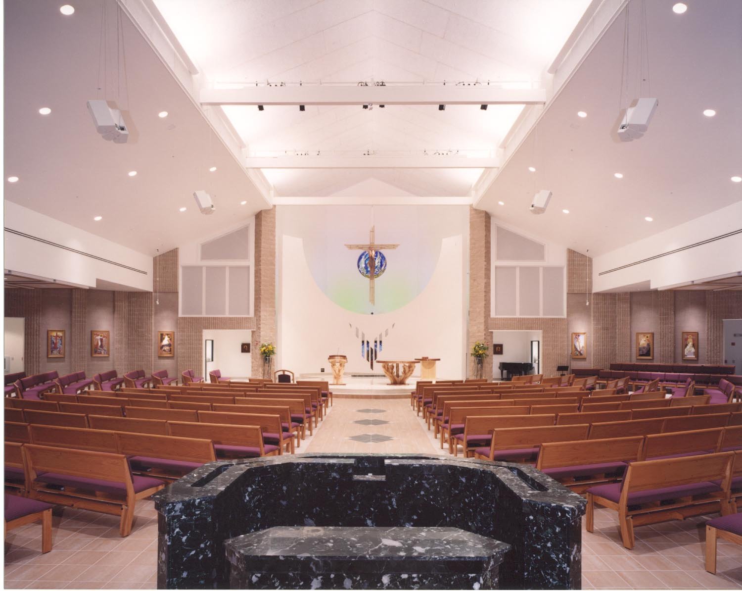 The sanctuary from behind the font: timber crucifix, ambo and altar on a raised curved platform.