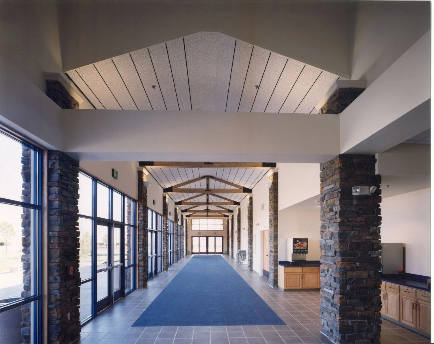 The lobby down its length, stone faced piers under a raised plank ceiling with exposed timber trusses at the far end.
