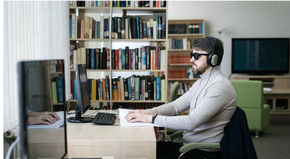 Blind professional using a computer and headphones in a library workspace.