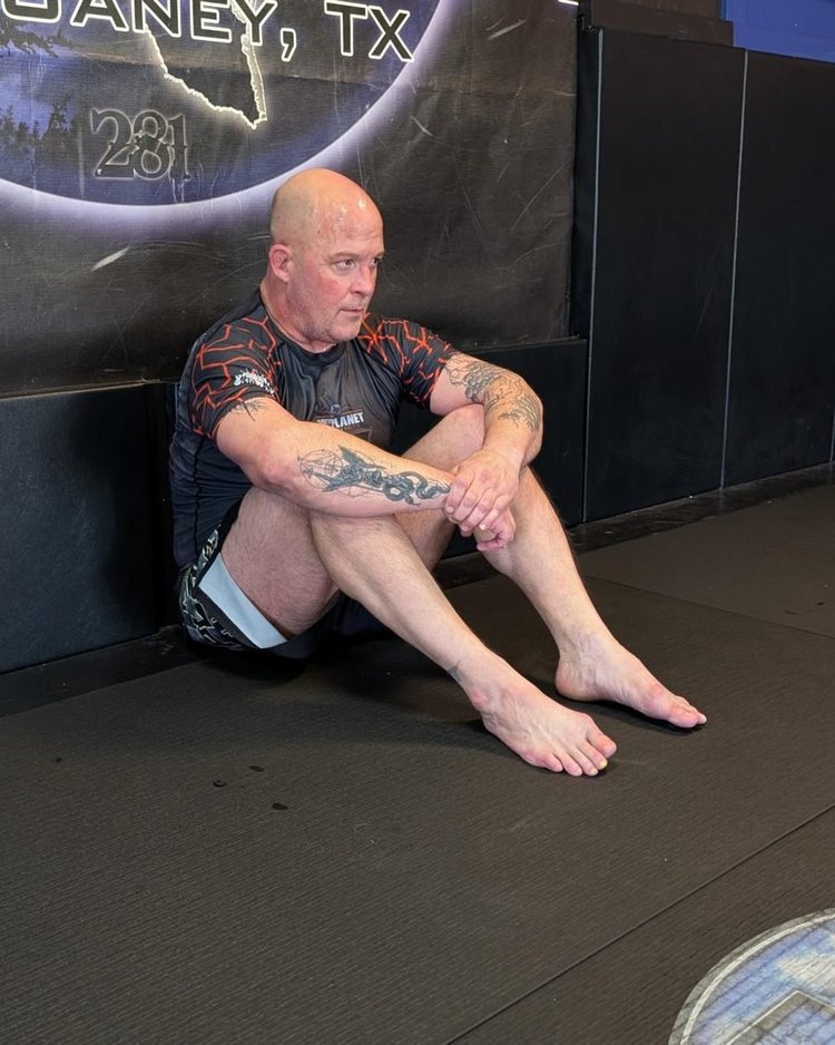 Rod Henderson sitting against the wall on the mats, watching training