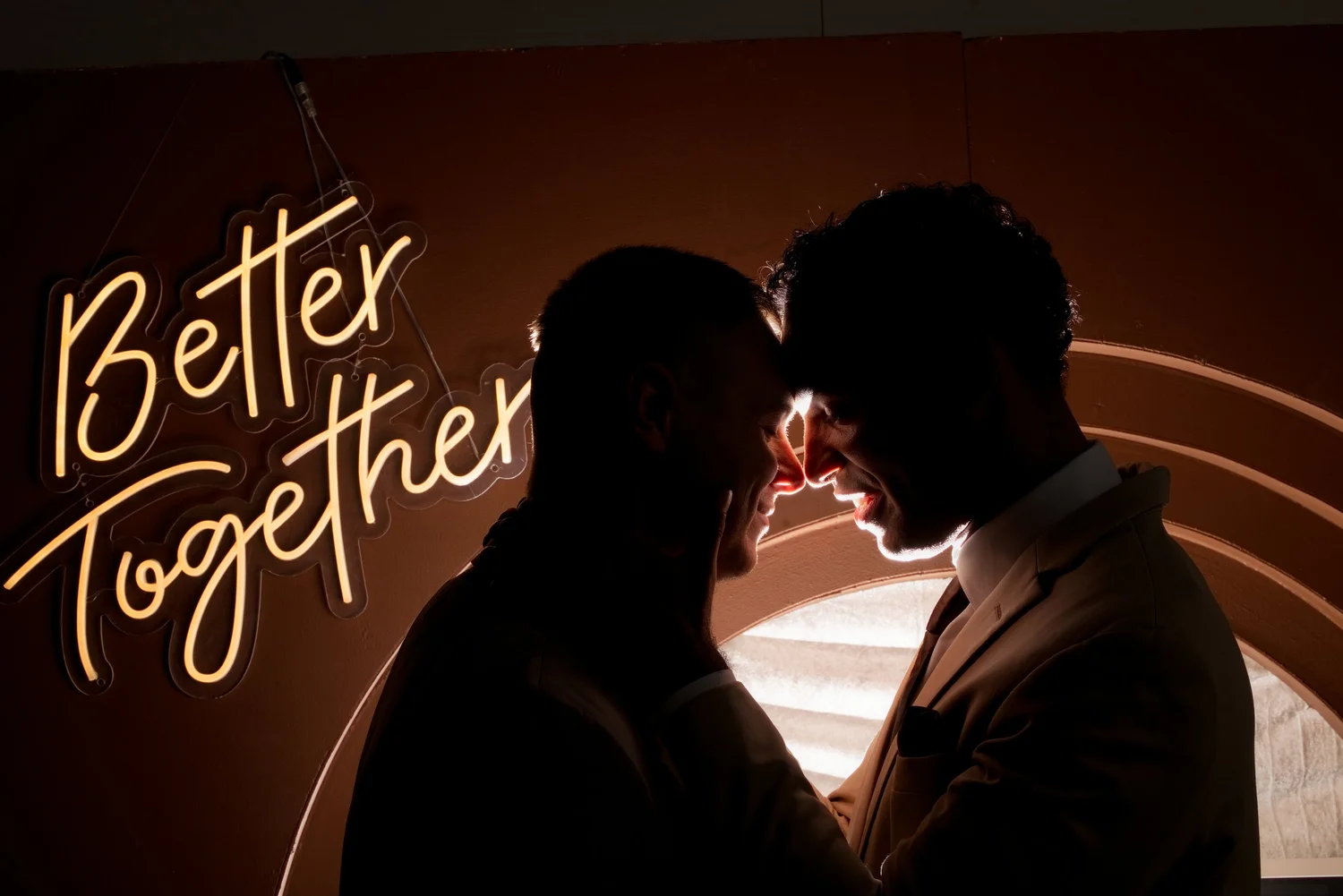 A couple silhouetted against a glowing Better Together neon sign