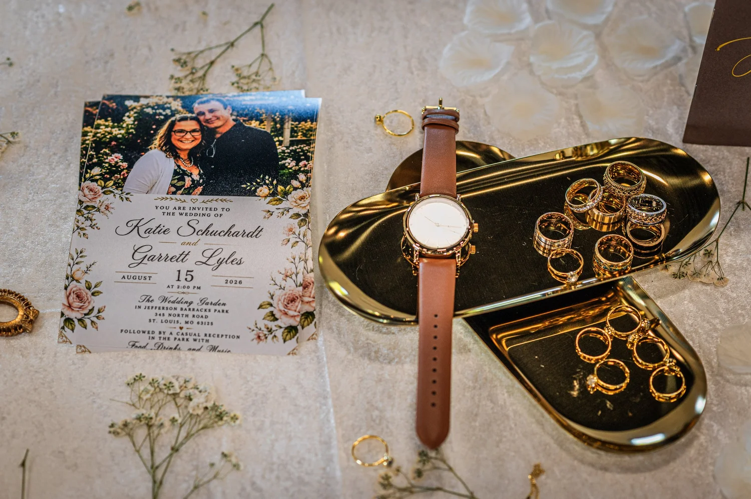 A wedding invitation, watch and rings arranged as a flat lay