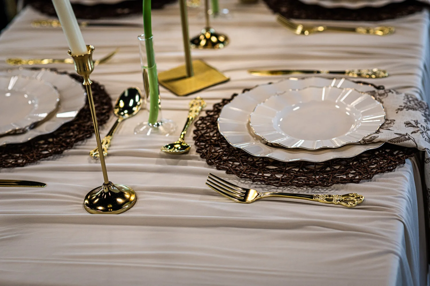 A candlelit place setting with gold flatware and ivory linens