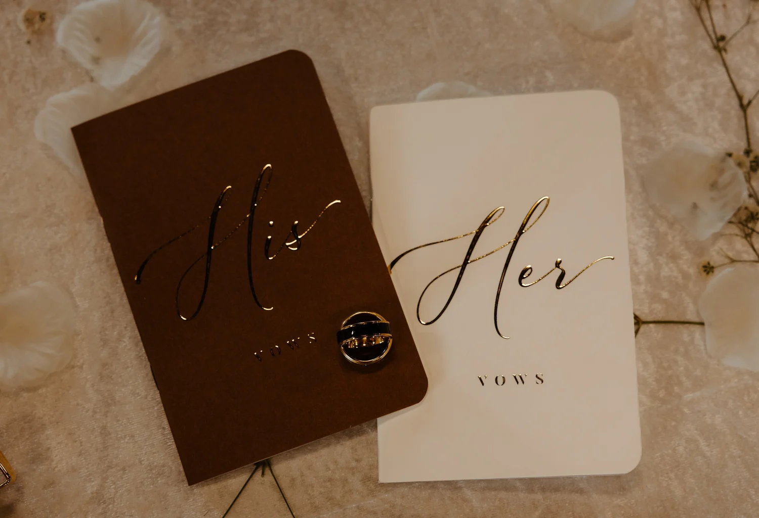 Ivory and chocolate his and her vow books with wedding rings and delicate white florals
