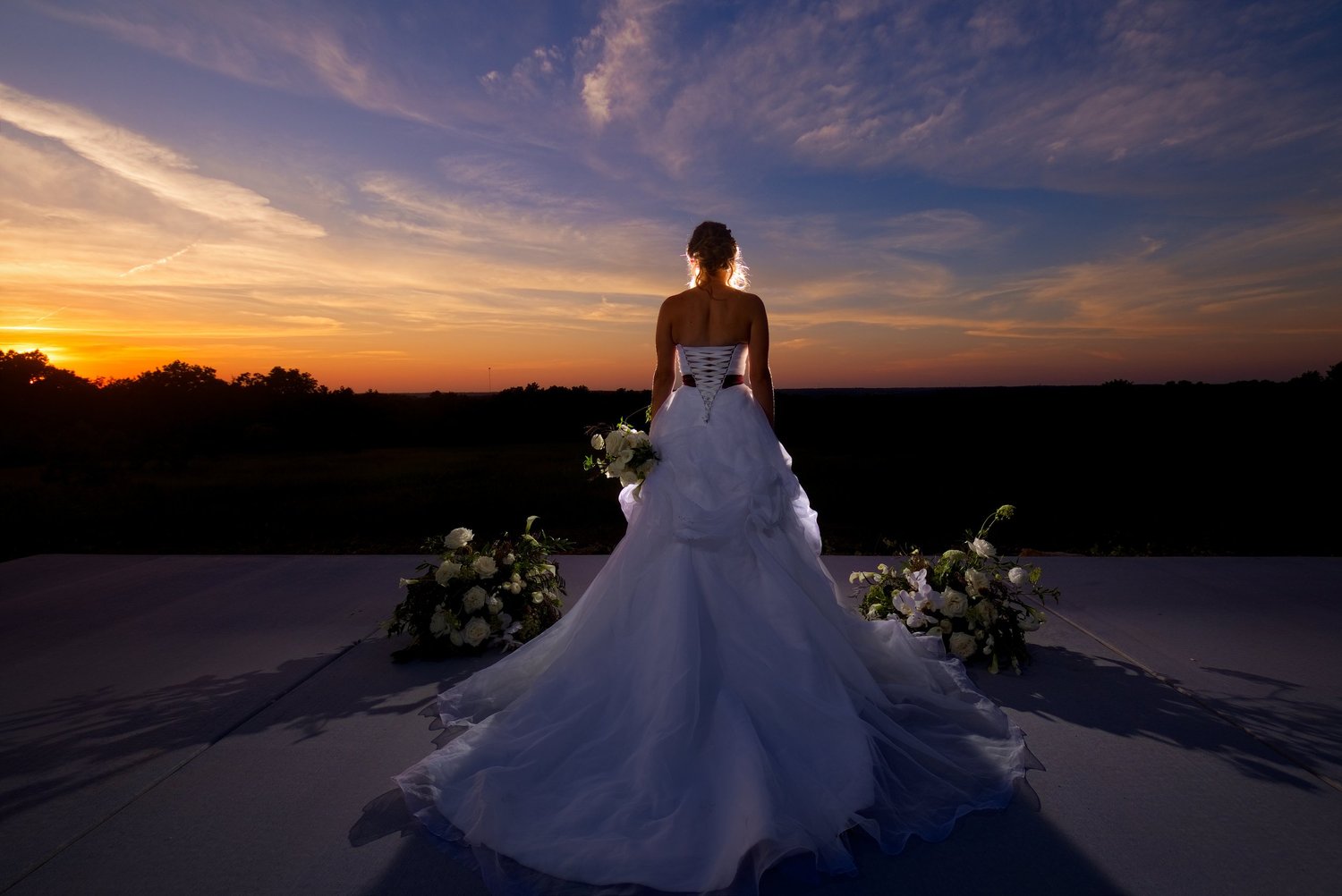 A bride in a white gown beneath a dramatic sunset