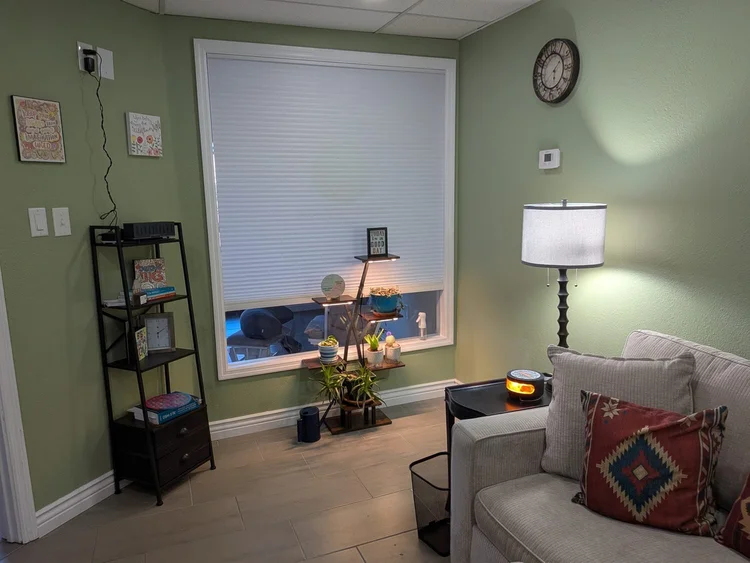 A cozy corner of Amy's office with a bookshelf, warm lamp, plants, and a chair by the window