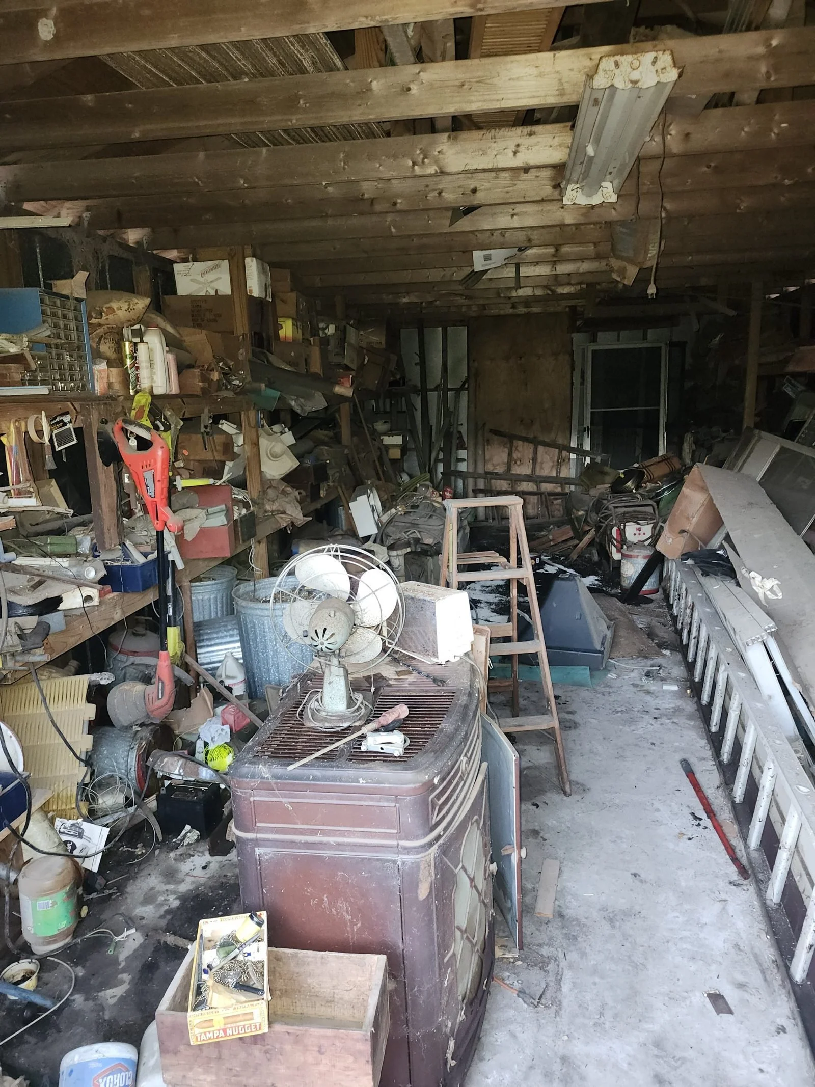 Shed crowded with tools, fans and household junk before the cleanout.