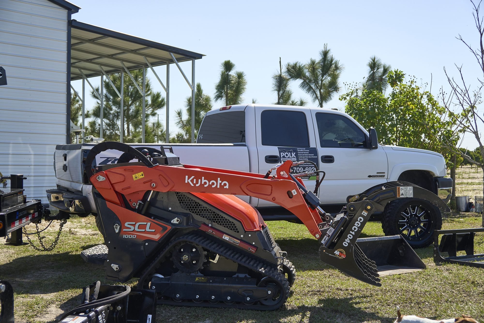 The Polk Services branded truck and orange Kubota SCL1000 mini skid steer staged for driveway and land work.