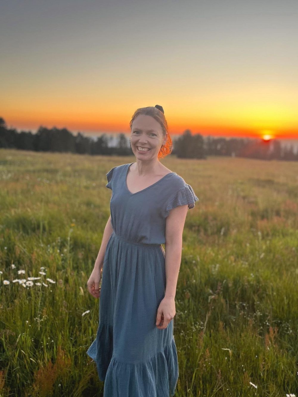 Dr. Abigail Stephens smiling in a blue dress, standing in a wildflower meadow at sunset in Oregon.