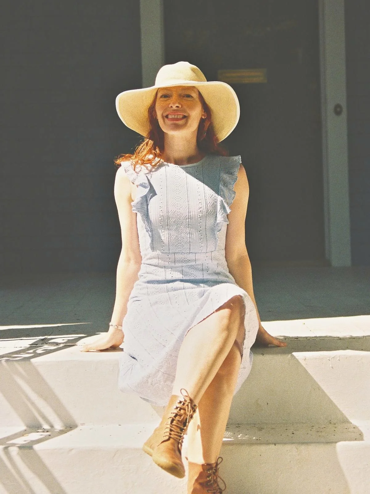 Dr. Abigail Stephens smiling in a straw sun hat and blue dress, seated on the front steps.