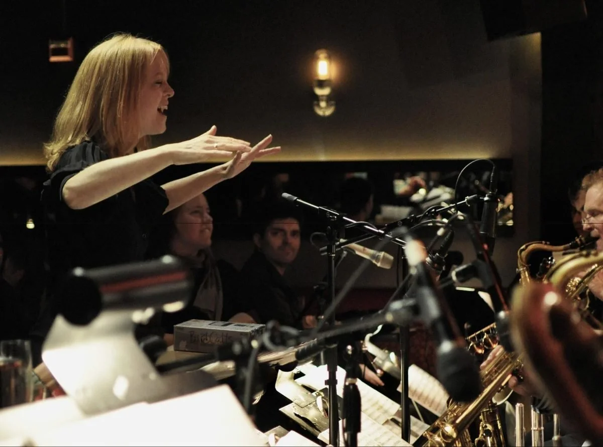 Maria Schneider conducting, arms outstretched and smiling