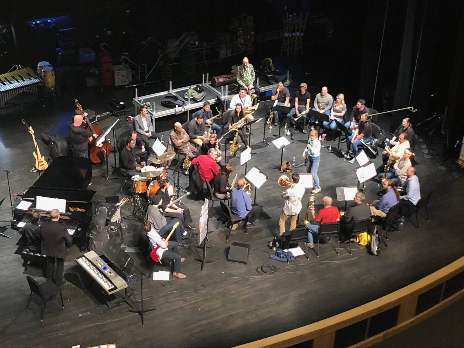 Maria Schneider leading a clinic on stage, with the ensemble seated in a circle around her
