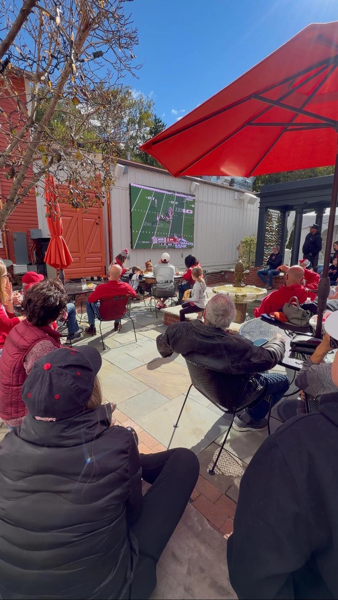 Guests seated around the courtyard fountain watching Ohio State football beneath a red umbrella.