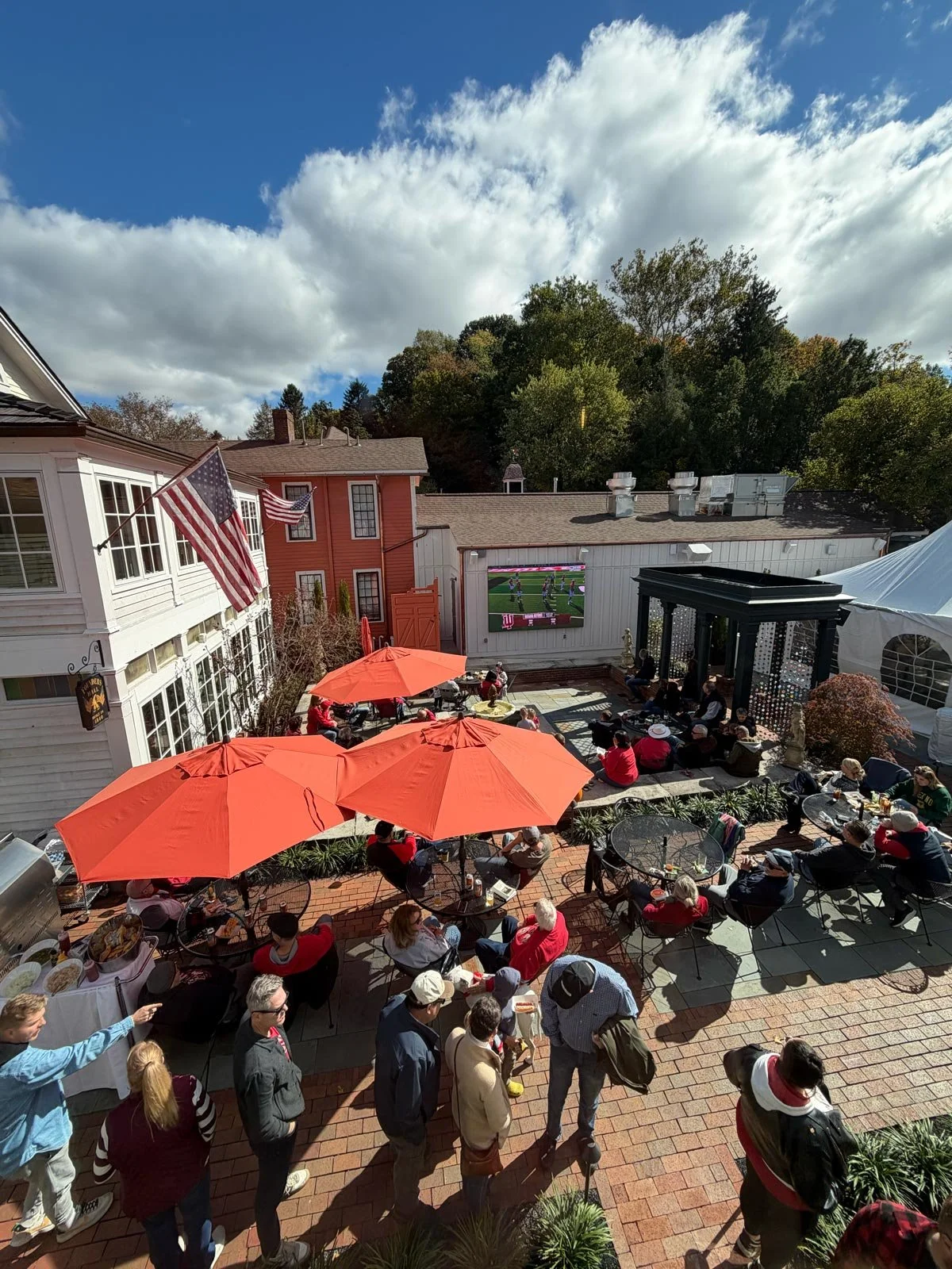 Guests gather beneath red umbrellas to watch football on the outdoor screen in the Buxton Inn courtyard.