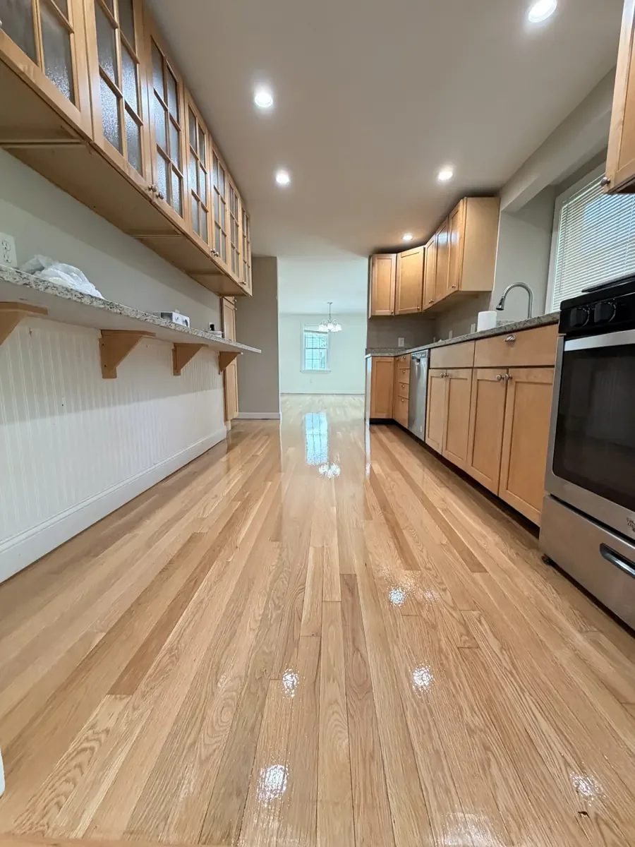 Finished hardwood floor running through a kitchen with wood cabinets.