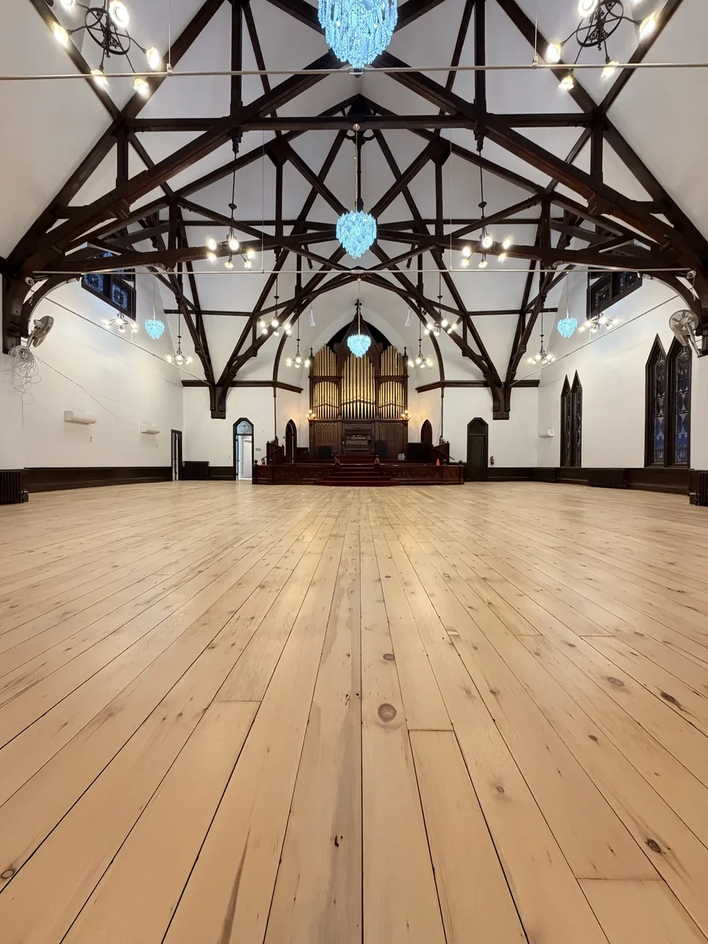 Symmetrical church interior with chandeliers, timber beams, and hardwood flooring