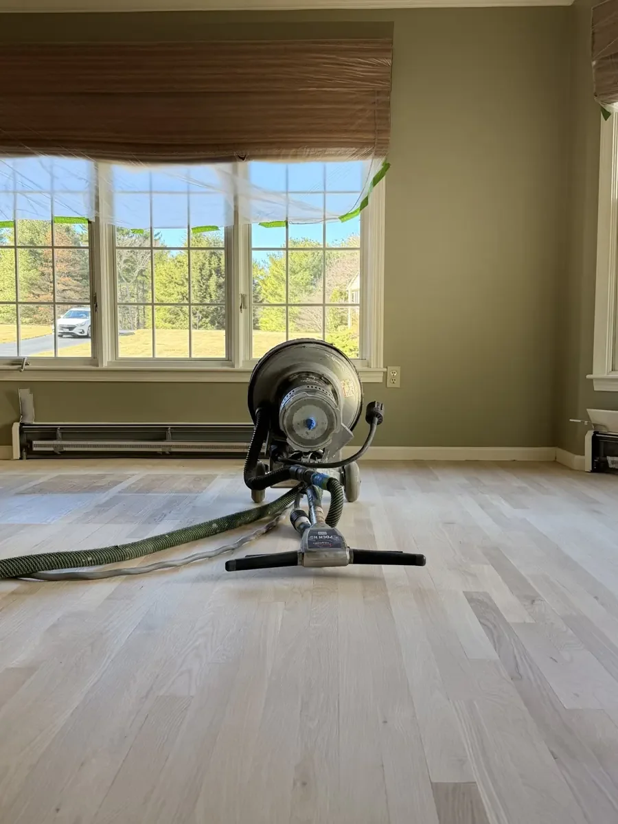 Floor sanding machine connected to a collection hose in front of a window.