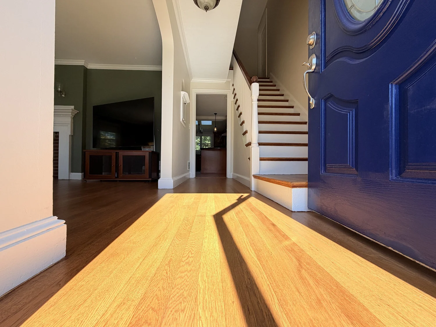 Refinished hardwood entry floor beside a blue front door