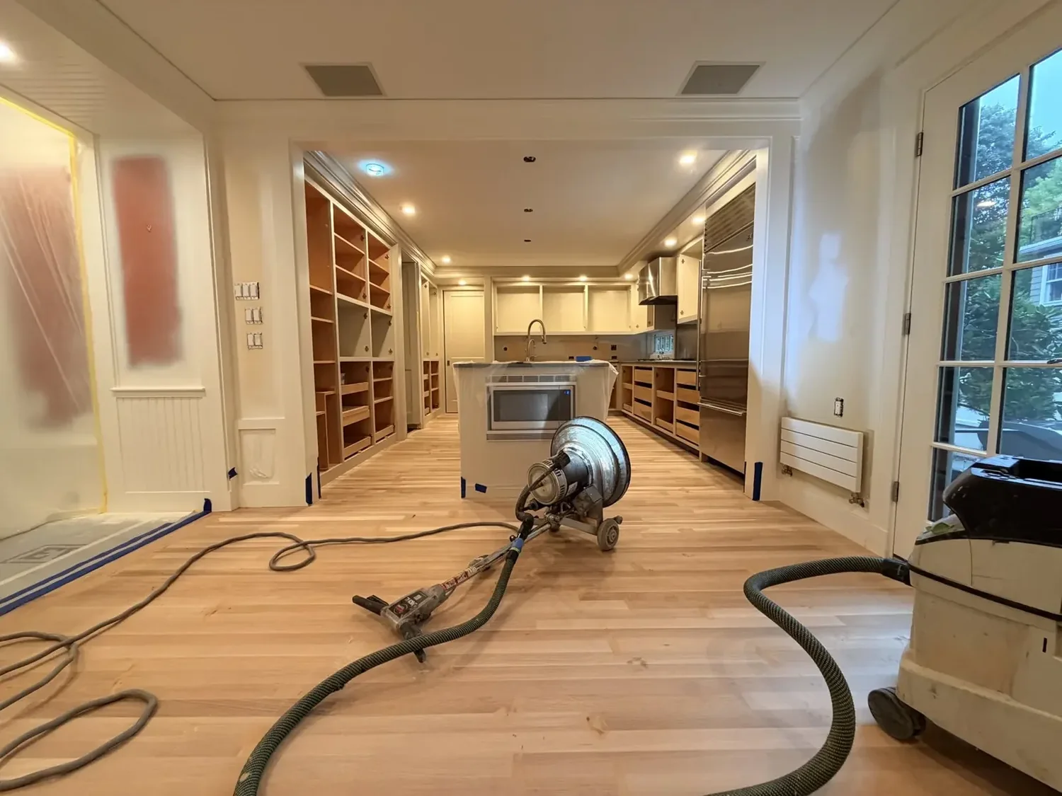 Sanding machine and connected hose beside a dust collector, with built-ins covered in protective sheeting.