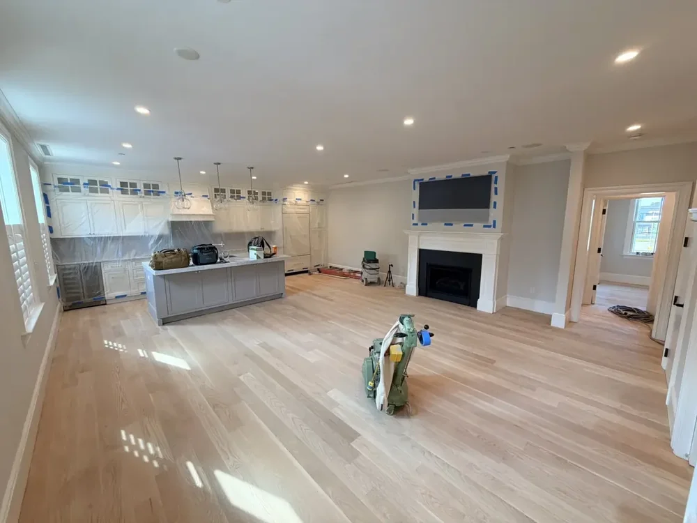 Light sanded wood floor in an open room with a floor machine and covered kitchen surfaces.