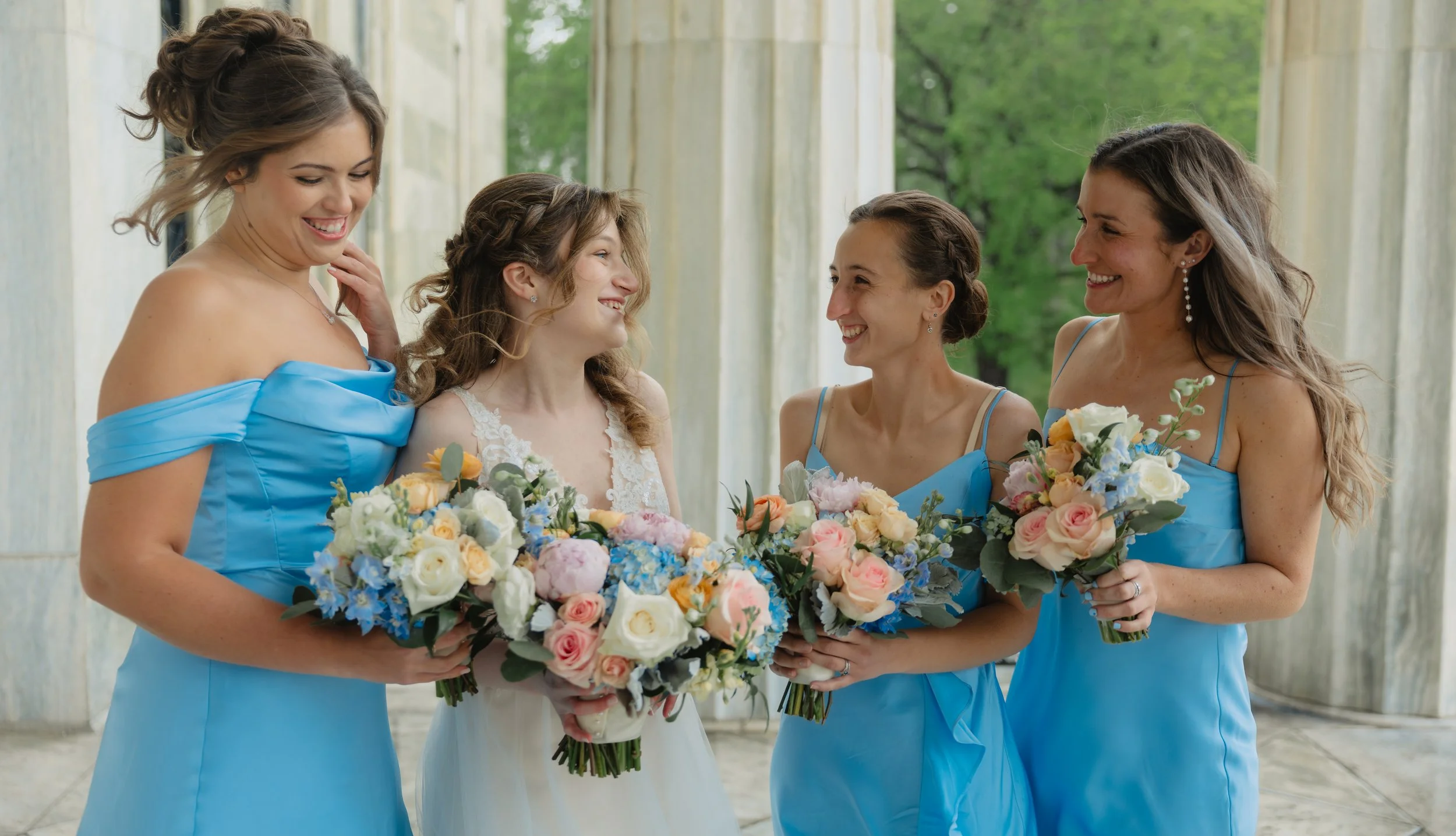 The bride laughing with her bridesmaids, bouquets in hand