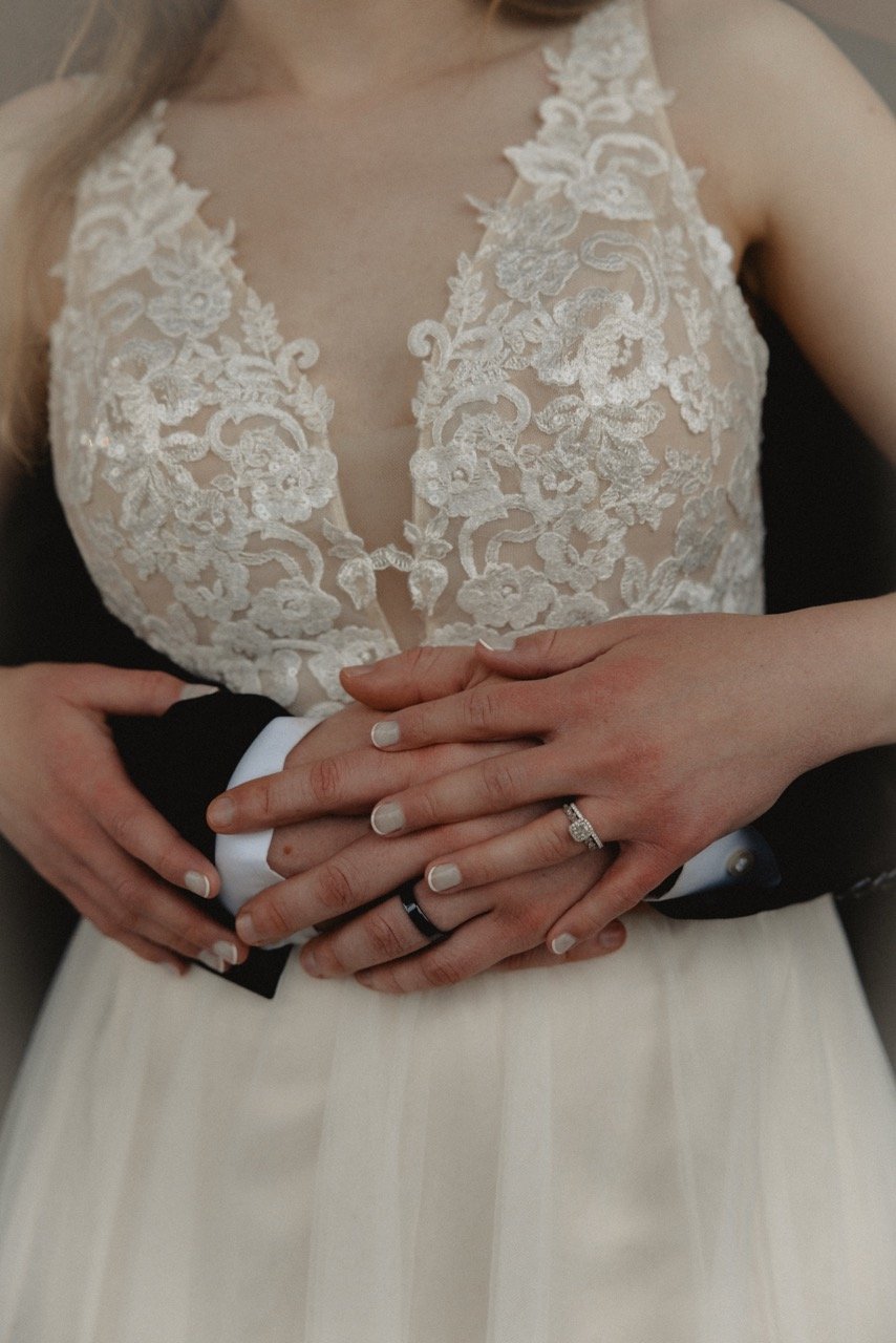 Hands with wedding rings resting on a lace dress