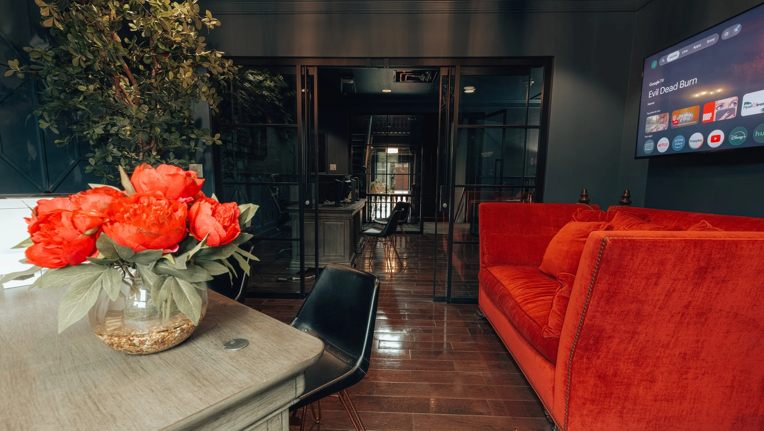 Red peonies on a table beside a red velvet sofa
