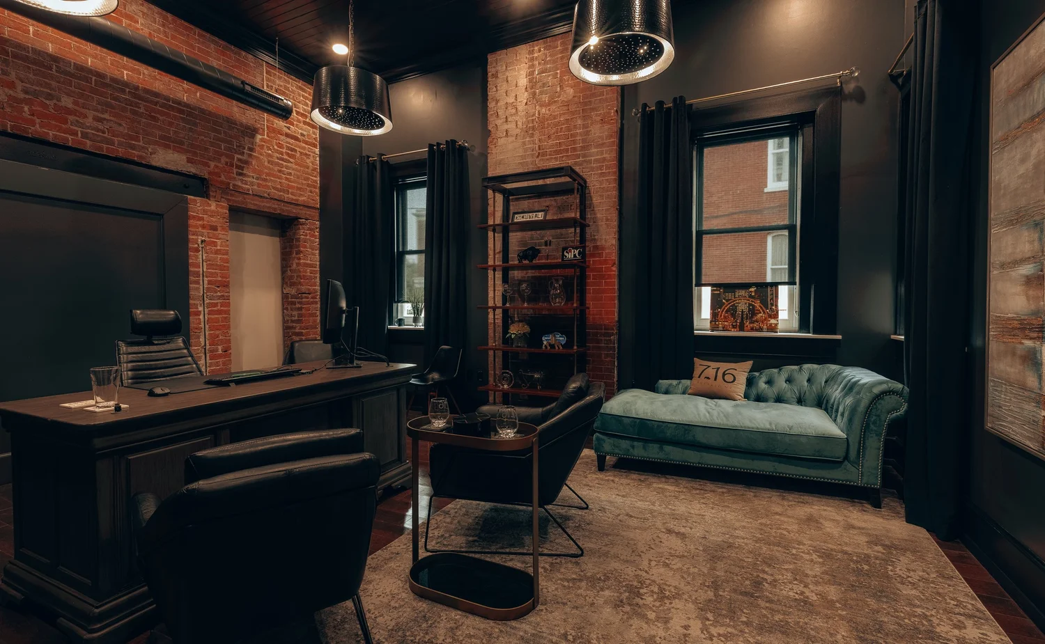 An office with a desk and a teal tufted sofa