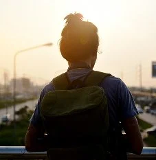 A teenager with a backpack looking out over a road at sunrise