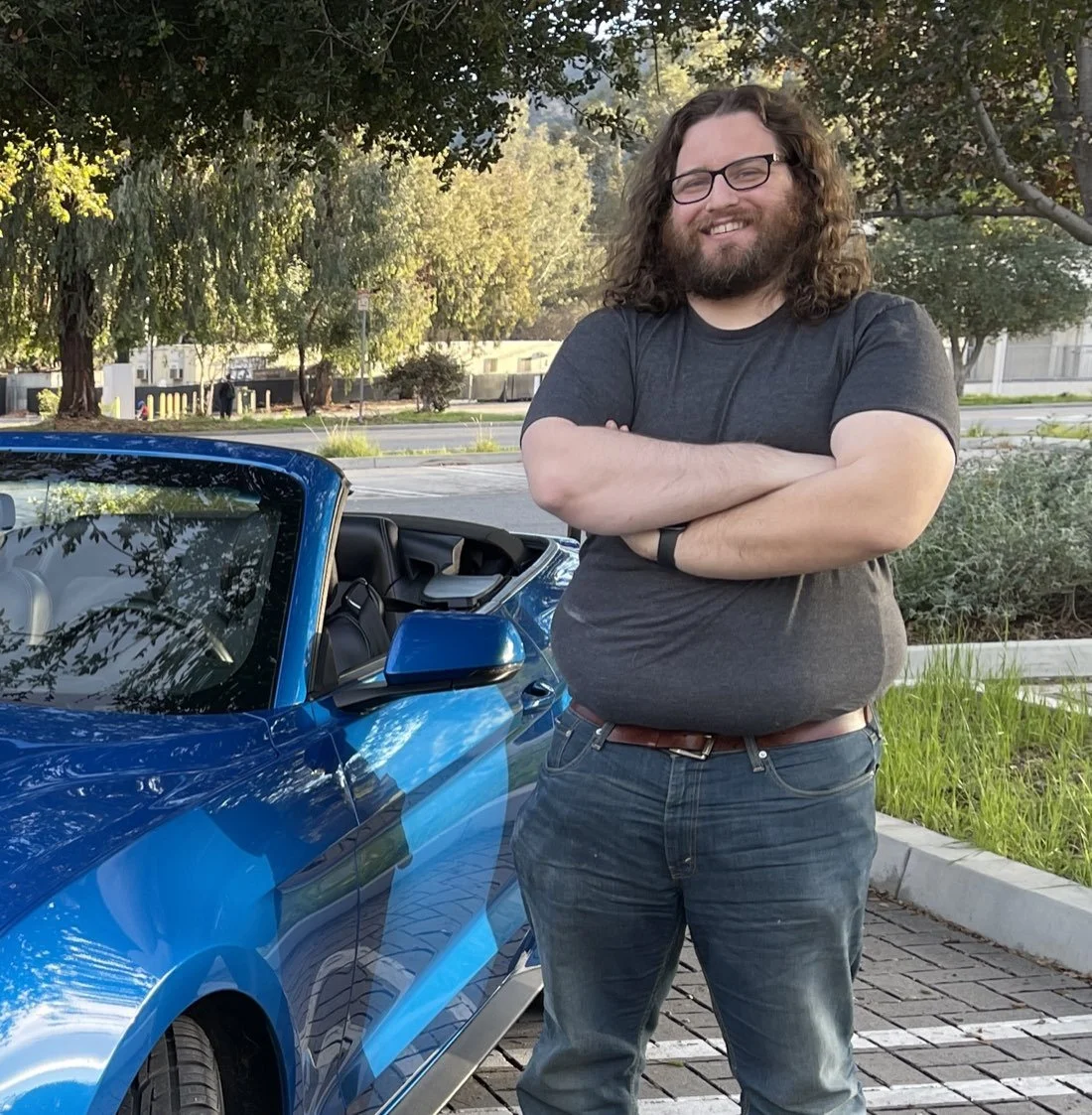 Travis standing next to a bright blue Ford Mustang convertible from the fleet