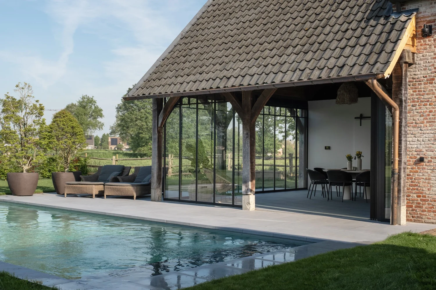 Poolhouse met pannendak naast een bakstenen woning in Nijlen, glazen wanden aan het zwembad