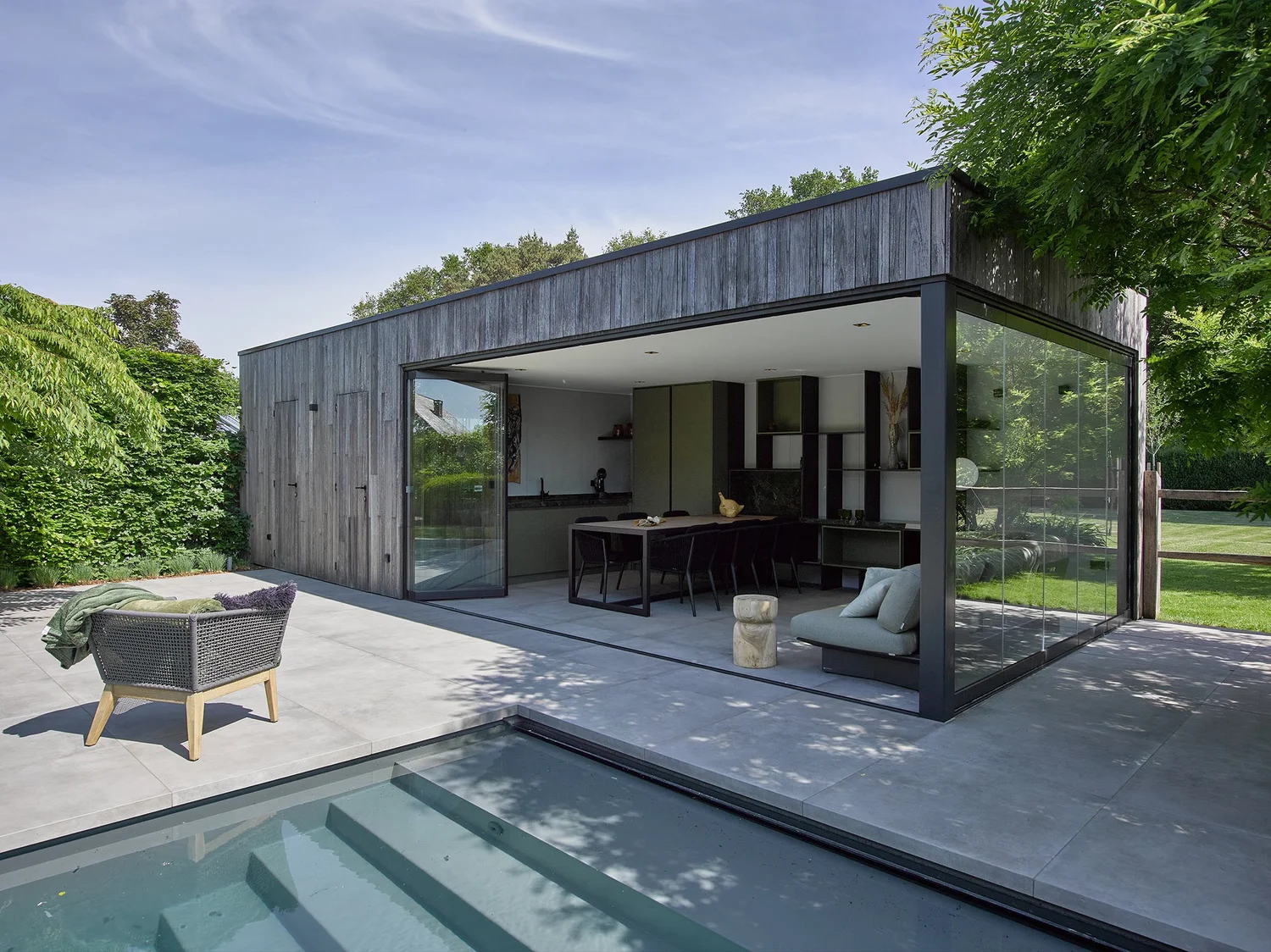 Poolhouse met donkere houten gevel in Zutendaal, de draaibare schuifwand staat open naar het zwembad
