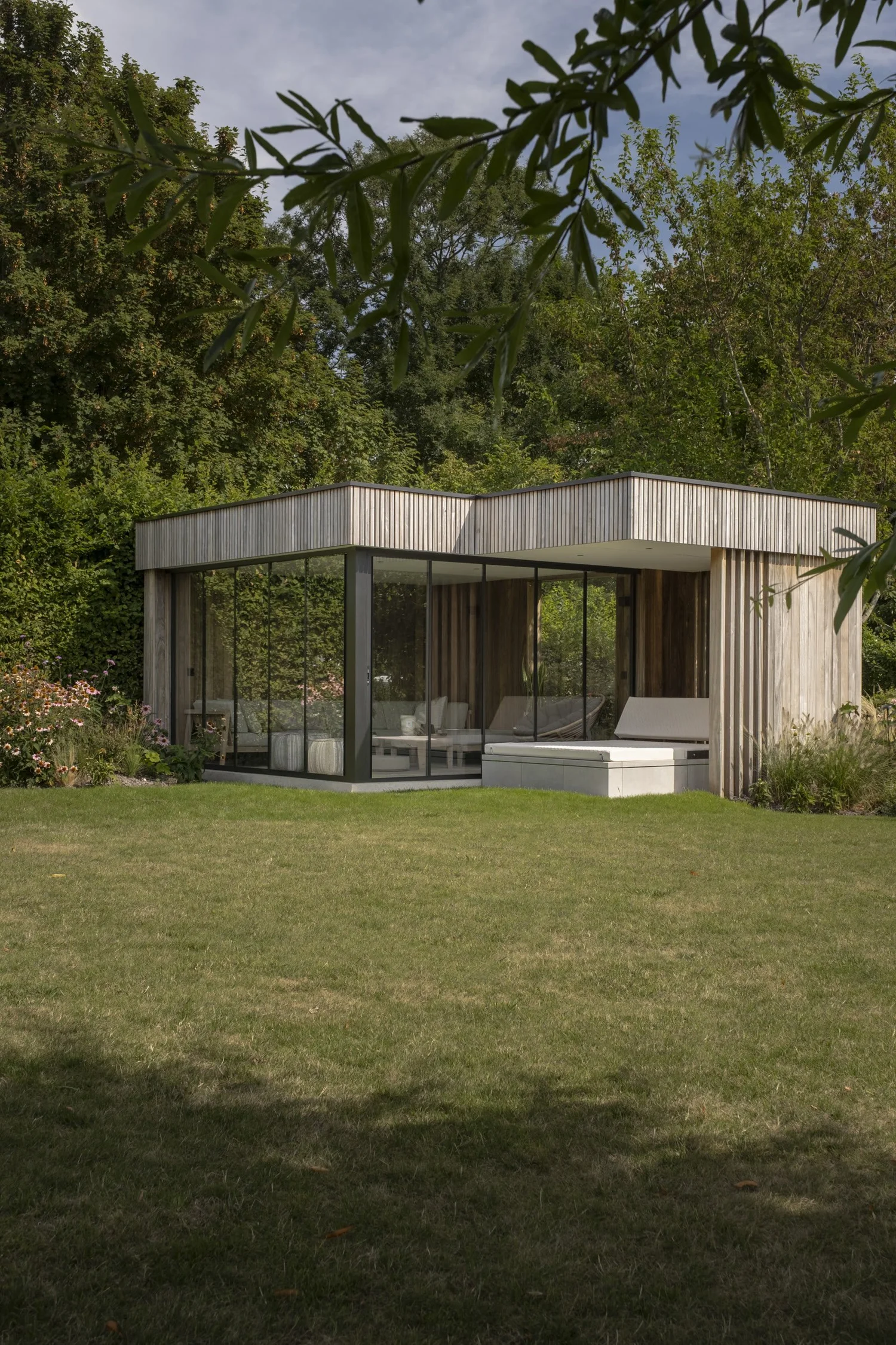 Tuinkamer met houten gevel achteraan een tuin in Wemmel, met glazen schuifwanden