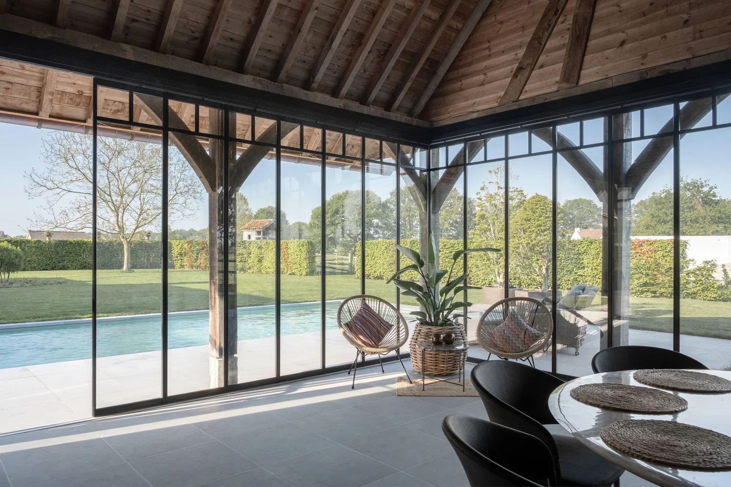 Binnenzicht van een poolhouse met houten spanten in Nijlen, glazen wanden met zicht op het zwembad