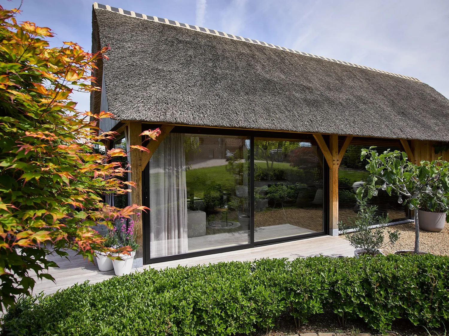 Bijgebouw met rieten dak in Bilzen, met een glazen schuifwand met dubbel glas tussen de houten staanders