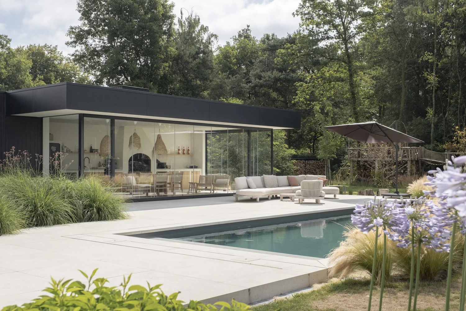 Modern poolhouse met zwart dak in Genk, loungehoek en zwembad voor de glazen wand