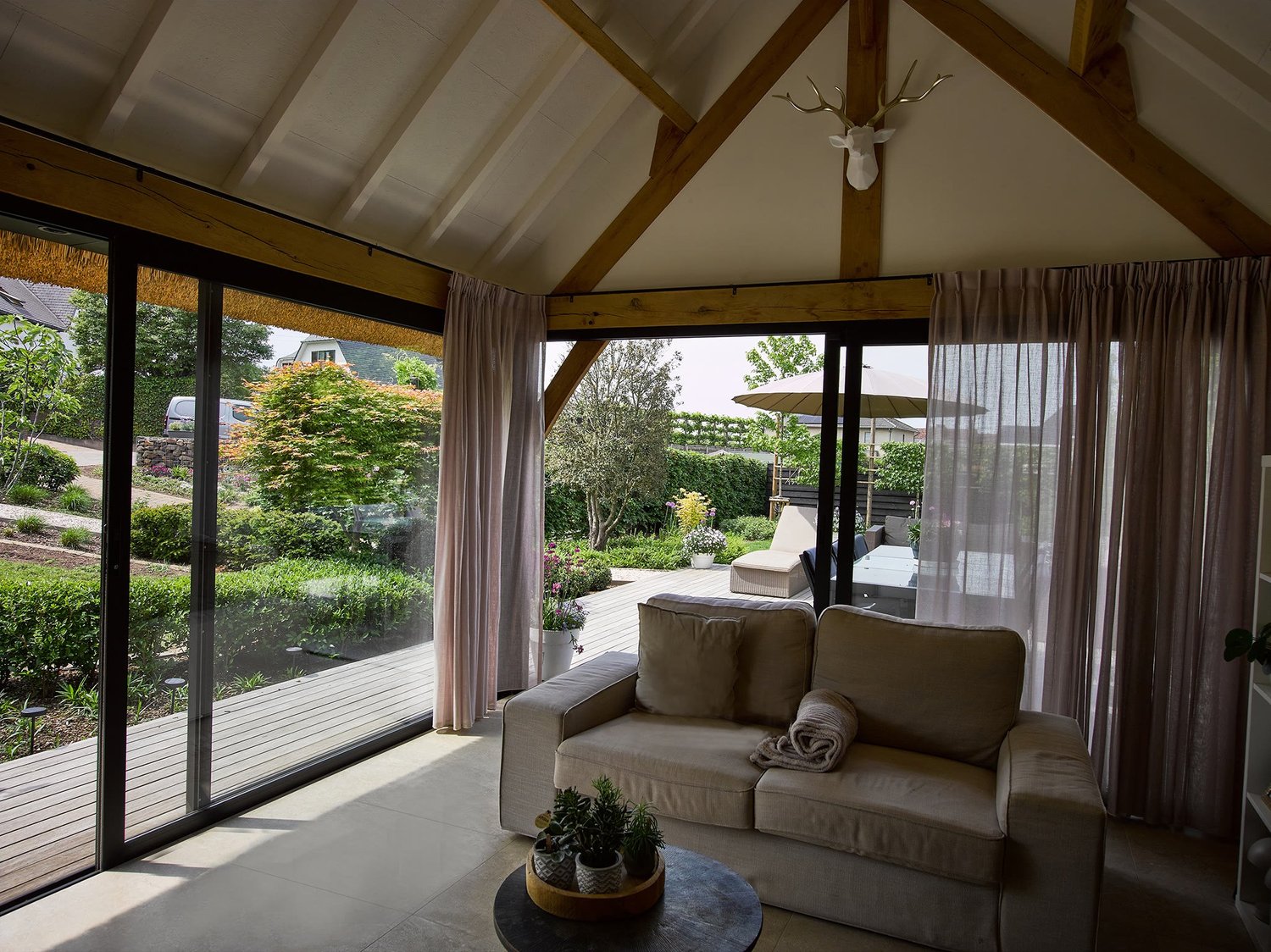 Binnenzicht van een bijgebouw met rieten dak in Bilzen, zetel en glazen schuifwanden met zicht op de tuin
