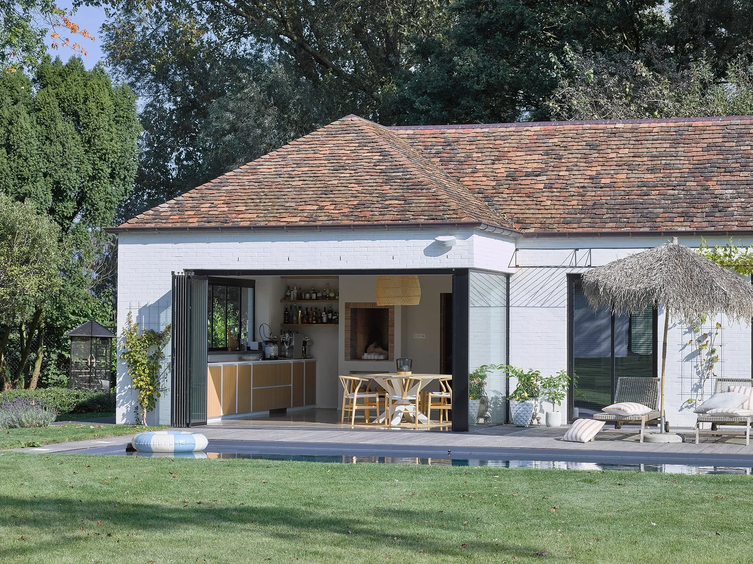 Wit poolhouse met pannendak in Sint-Gillis, de glazen wanden staan open naar de tuin en het zwembad