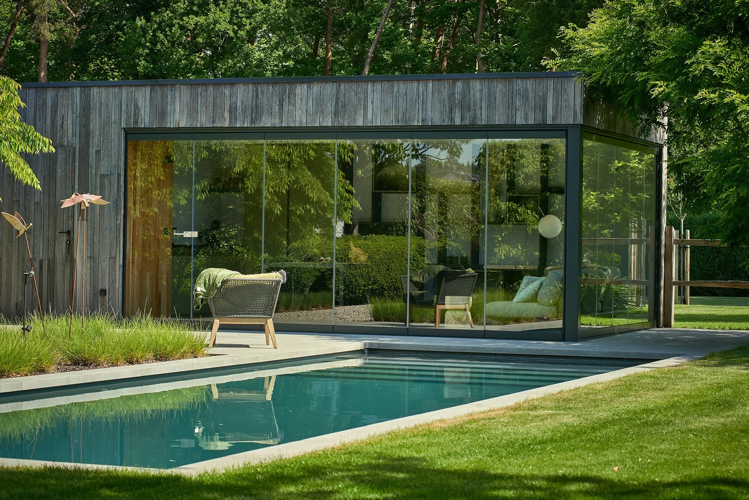 Poolhouse met donkere houten gevel en glazen wand aan een zwembad in Zutendaal