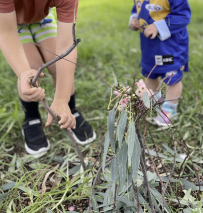 Children building a small stick house on the grass with leaves and bark