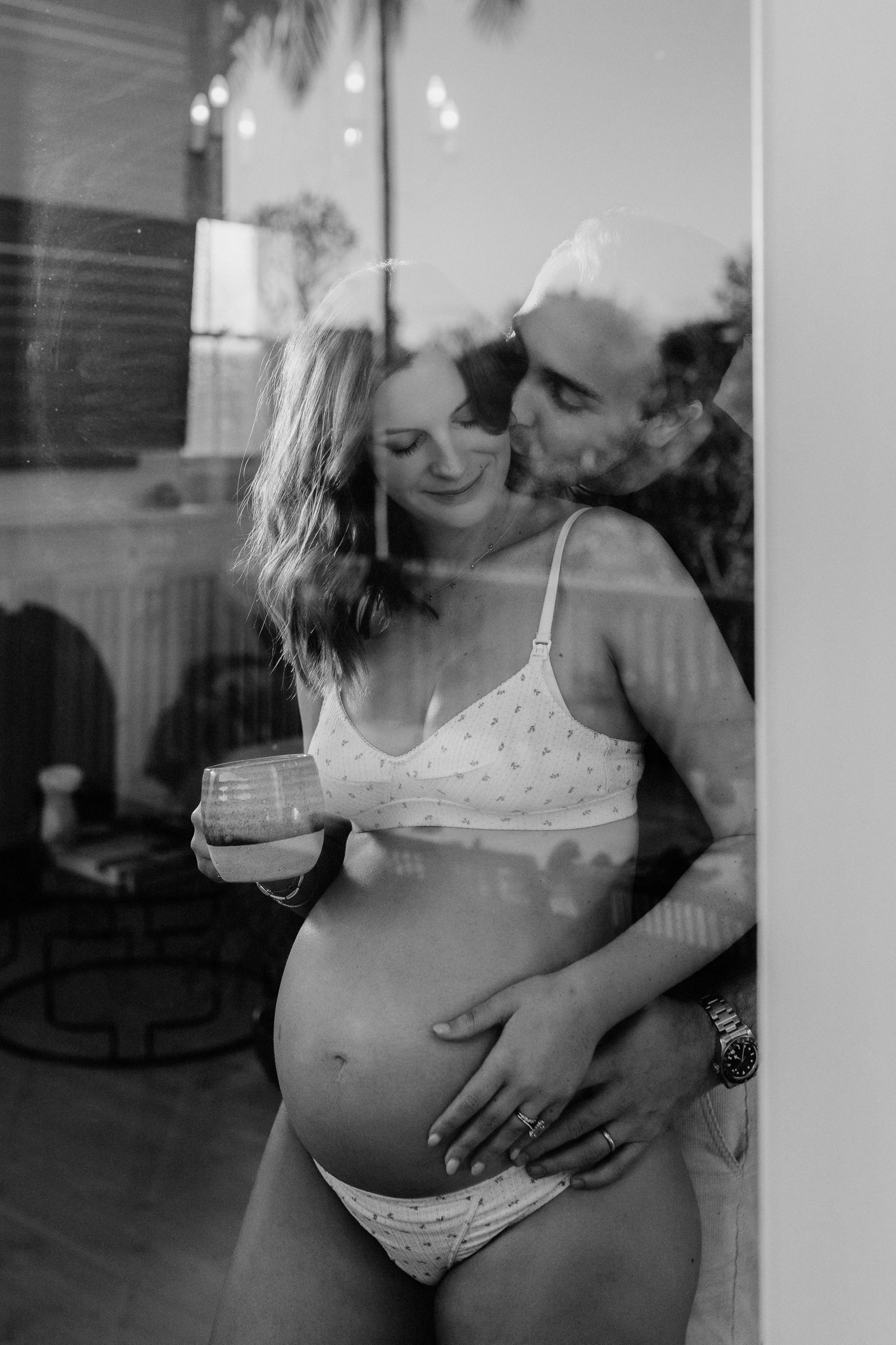 A couple embracing, her pregnant belly visible, photographed by Bridget Wood