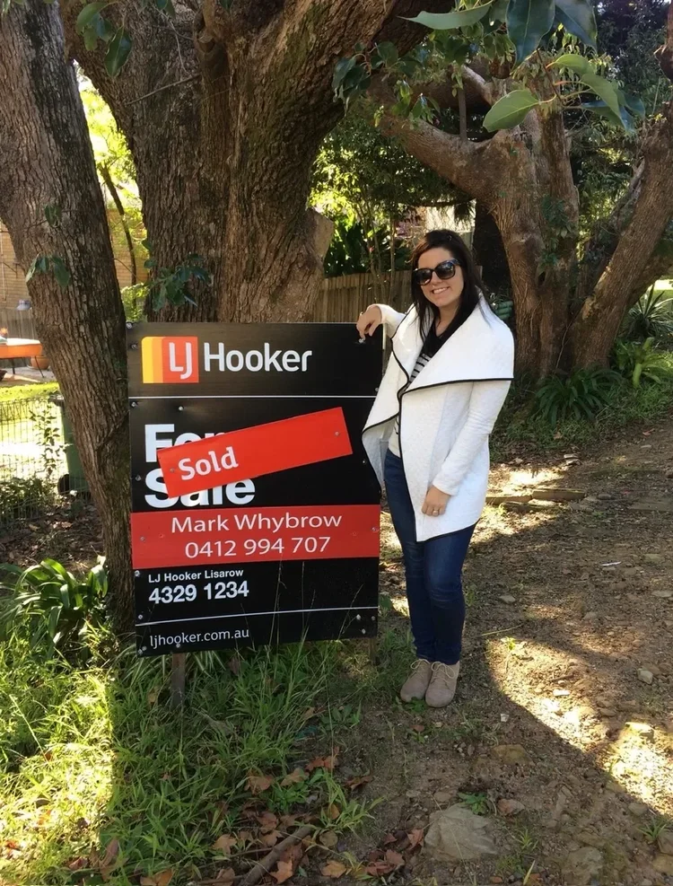 Stina standing beside a Sold sign at one of her own properties