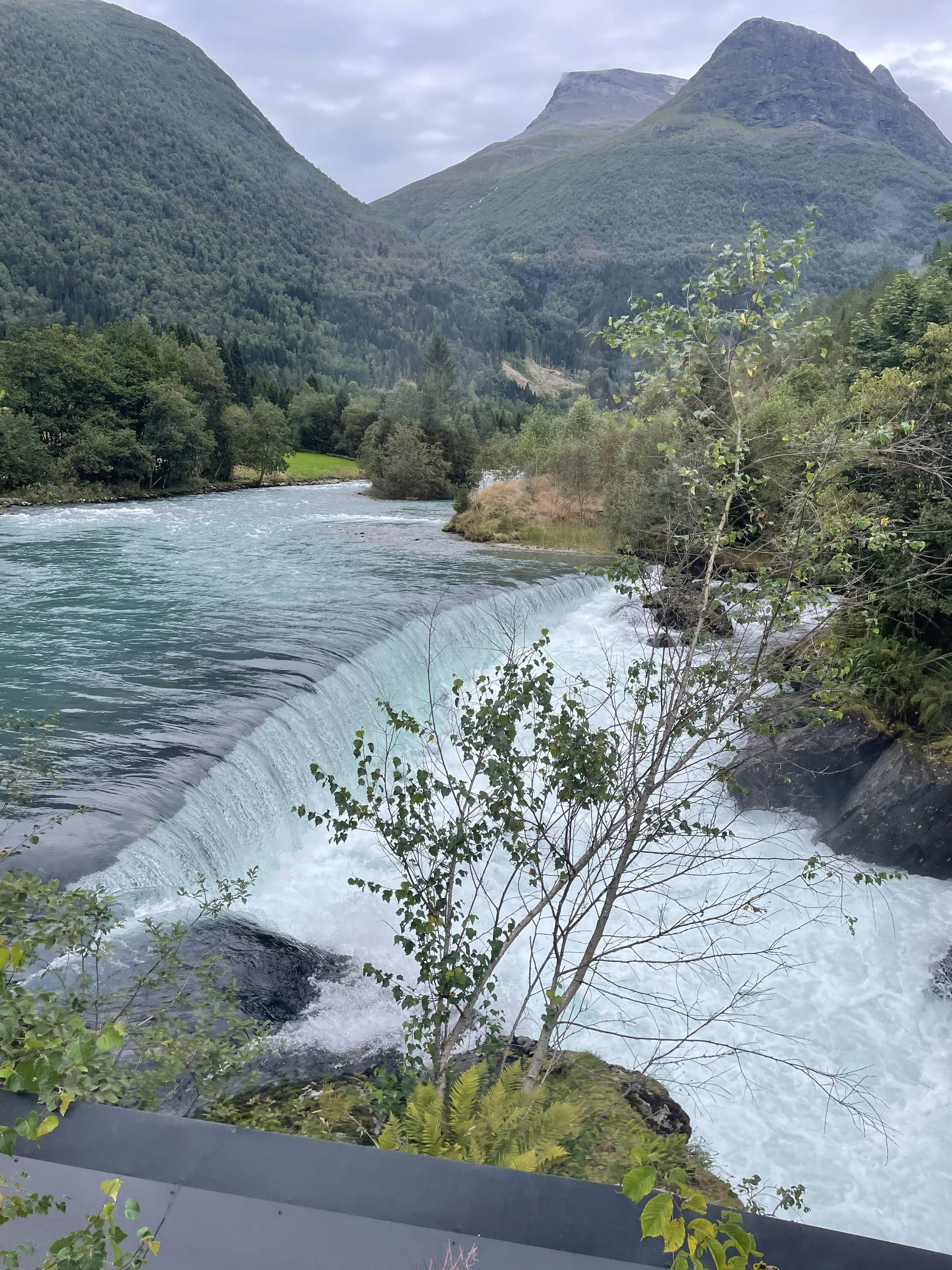 A turquoise glacial river rushing through a mountain valley.