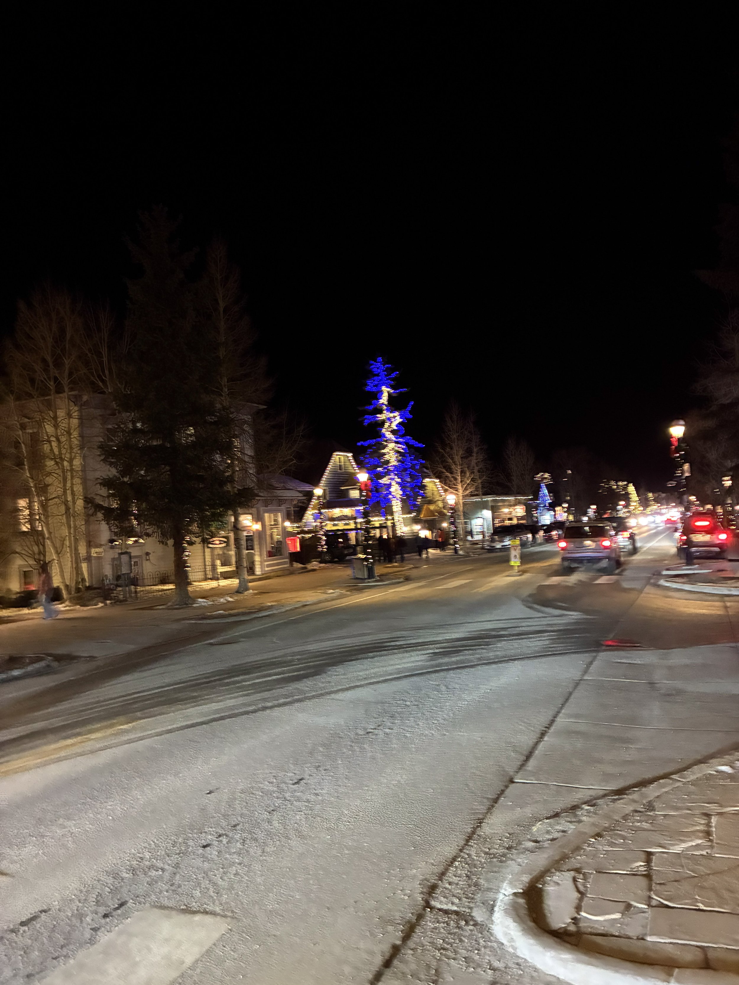 A Christmas tree glowing blue on a night street.