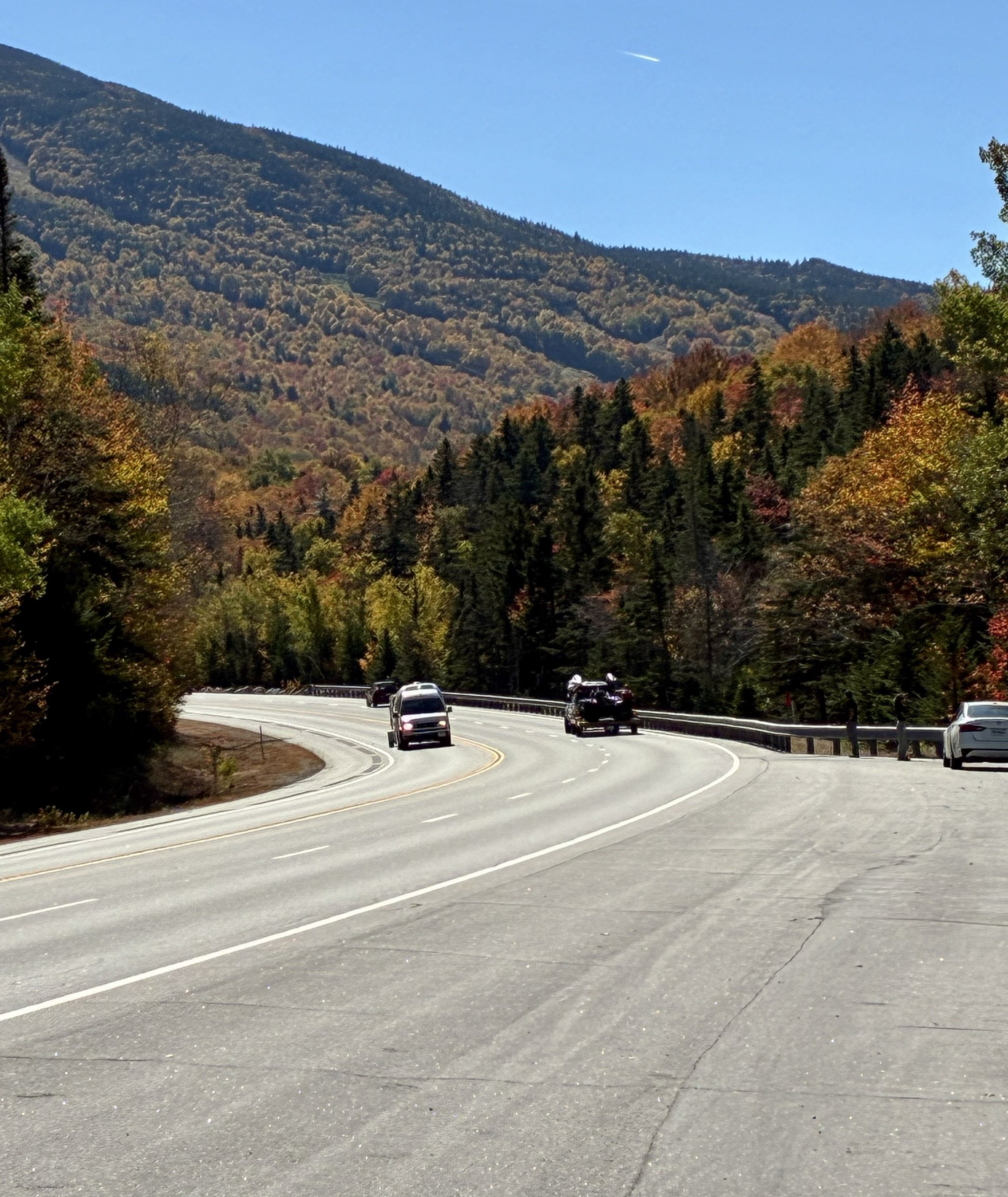 A highway curving toward a red and orange foliage-covered mountain.